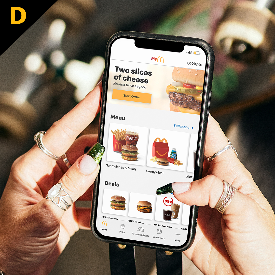 Customer holidng cell phone with McDonald's app on screen. The letter "D" in the top left corner. 