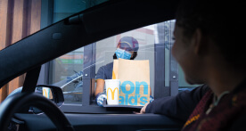 Masked McDonald's employee handing customer order through takeout window